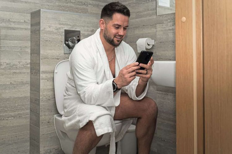 Mann mit Smartphone in der Hand auf Toilette.