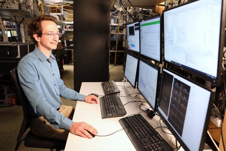Quantenphysiker Martin Ringbauer arbeitet am PC und hat drei Tastaturen und sechs Bildschirme vor sich.