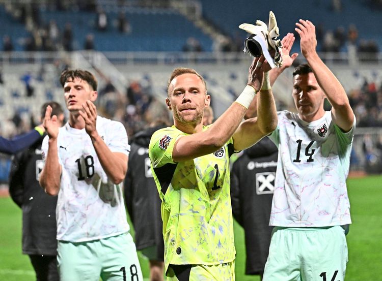 Drei Fußballspieler der österreichischen Nationalmannschaft klatschen nach einem Spiel auf dem Spielfeld in die Hände, darunter der Torwart in einem leuchtend gelben Trikot. Im Hintergrund sind verschwommene Zuschauertribünen zu erkennen.