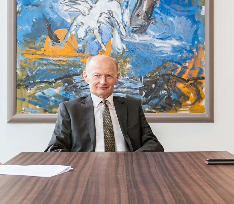 Franz Gasselsberger, Chef der Oberbank, sitzt an einem großen Schreibtisch, hinter ihm ein gelb-blaues Bild.