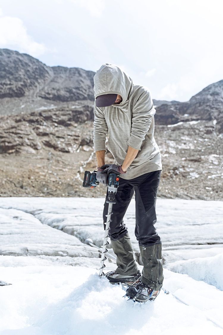 Eine Frau auf dem Gletscher bohrt ein Loch in das Eis