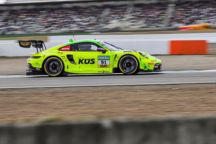 Ein neon-grüner Porsche 911 GT3 R Evo mit der Startnummer 91, gesponsert von KÜS, fährt während eines Rennens auf dem Hockenheimring in Baden-Württemberg, Deutschland. Zuschauertribünen sind im Hintergrund zu sehen.
