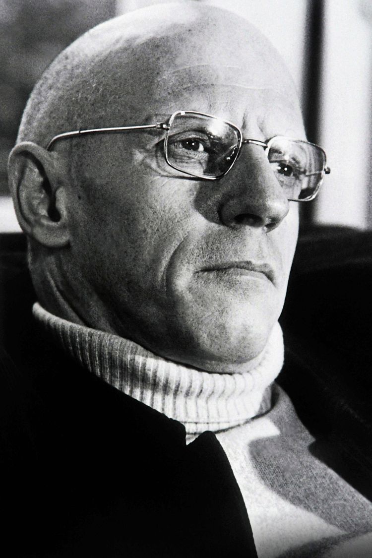 Schwarz-Weiß-Porträt eines Mannes mit Glatze und Brille, der einen Rollkragenpullover trägt. Er schaut ernst zur Seite.