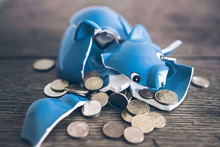 Ein blaues Sparschwein liegt zerschlagen auf einem Tisch. Ein paar Euro-Münzen waren im Sparschein.