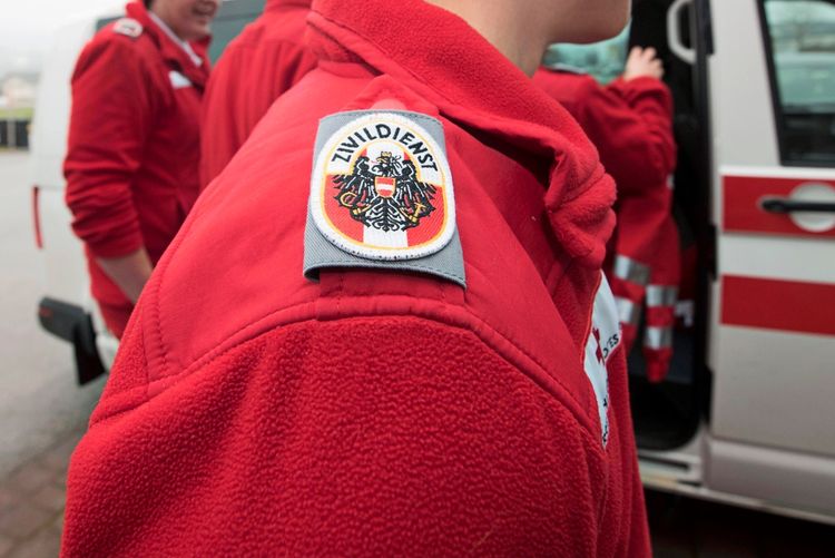 Ein Detailfoto zeigt die Schulter eines Menschen in roter Uniform mit dem Abzeichen 