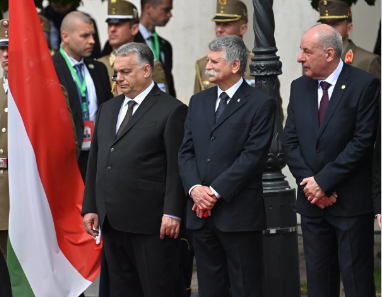 Die drei Männer stehen in Anzug nebeneinander. Die ungarische Flagge weht daneben.