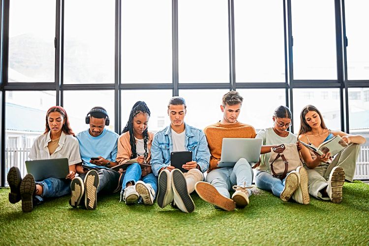 Junge Menschen sitzen vor einem Fenster mit Laptops.