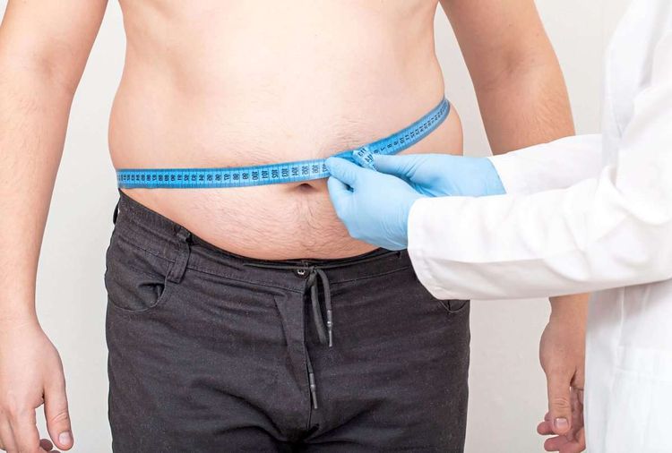 Ärztin misst mit blauem Maßband den Bauchumfang von einem Patienten