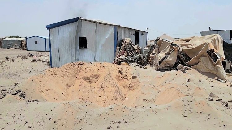 Beschädigte Metall- und Zeltbauten in einer sandigen, kahlen Umgebung des Mail al-Saila-Lagers für Binnenvertriebene am Rande von Marib, nach einem angeblichen Houthi-Raketenangriff. Im Hintergrund sind weitere Bauwerke und Rauch sichtbar.