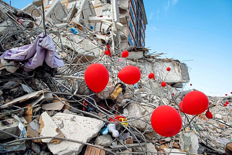 Trümmer zerstörter Häuser, an denen rote Luftballons befestigt wurden