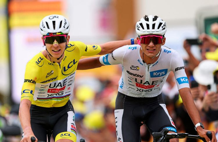 Zwei Radfahrer des Teams UAE Team Emirates jubeln am Ende der 20. Etappe der Tour de France 2026. Einer trägt das gelbe Trikot, der andere das weiße Trikot. Beide strahlen vor Freude, während der gelbe Träger dem weißen Arm auf die Schulter legt. Im Hintergrund sind Zuschauer zu sehen.