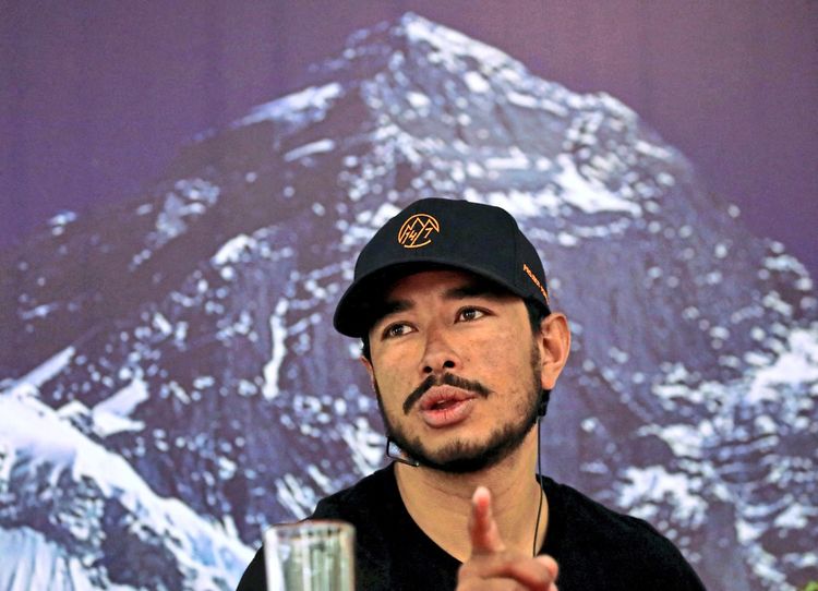 Ein Mann mit schwarzer Kappe spricht bei einer Pressekonferenz. Im Hintergrund ist ein schneebedeckter Berg zu sehen.