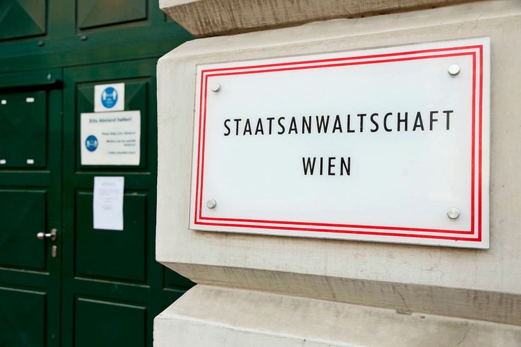 Hinweistafel mit der Aufschrift „STAATSANWALTSCHAFT WIEN“ an einer weißen Wand, daneben ein grünes Eingangstor mit weiteren Schildern.