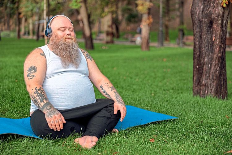 Bärtiger, tätowierter Mann mit Kopfhörer auf Yogamatte