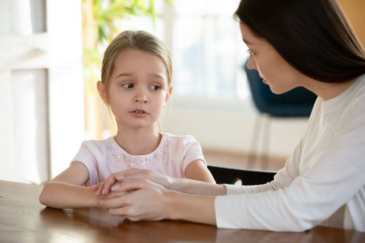 Ein kleines Mädchen mit besorgtem Gesichtsausdruck im Gespräch mit seiner Mutter, die seine Hände hält