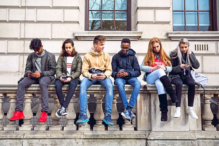 Eine Gruppe von Teenagern sitzt auf einer Wand - alle schauen auf ihr Smartphone.