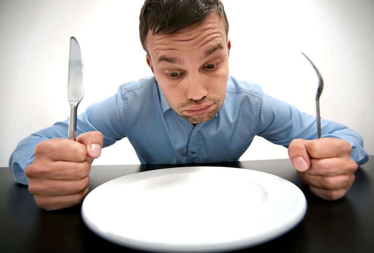 Mann mit Messer und Gabel vor einem leeren Teller, der auf Essen hofft