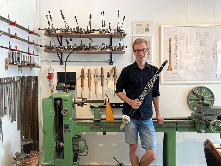 Junger Mann steht vor vielen Werkzeugen und hält ein Instrument in der Hand