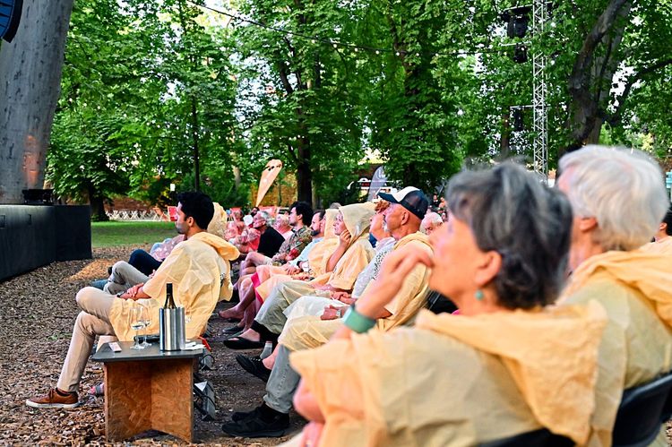 Personen in Regenponchos sitzen im Theater im Park in Wien.