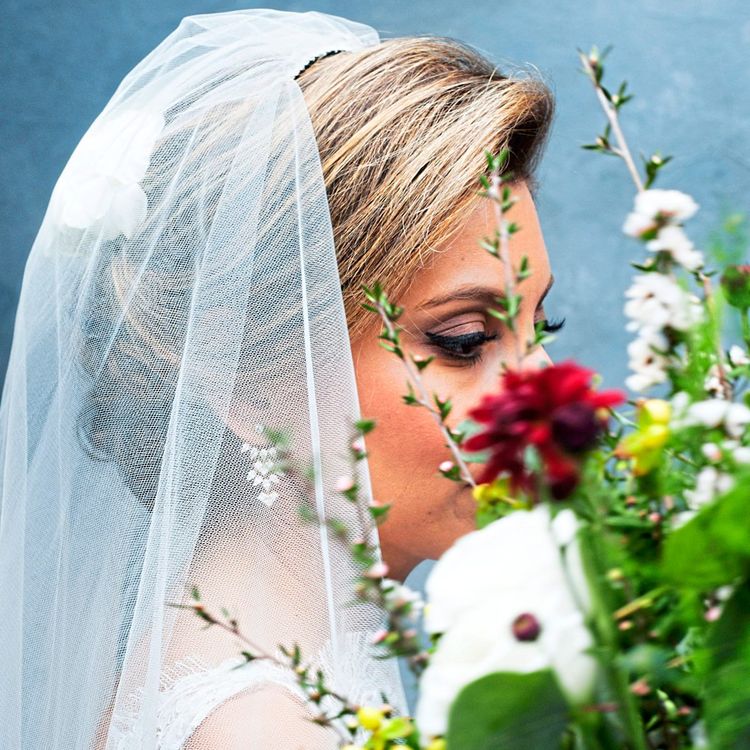 Eine Braut mit Schleier, deren Gesicht von der Seite zu sehen ist, riecht an einem Blumenstrauß