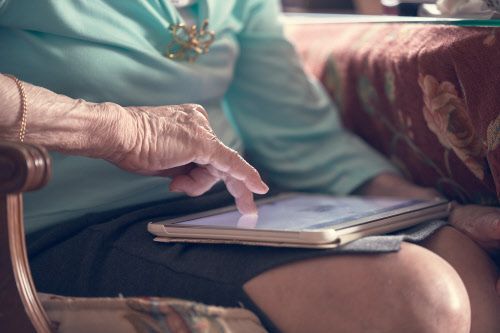 Eine ältere Frau tippt auf einem Tablet.