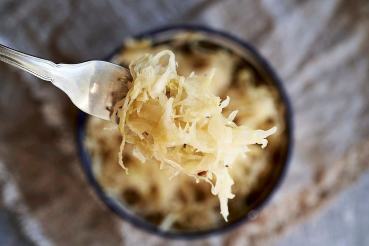 Nahaufnahme von Sauerkraut auf einer Gabel, von oben fotografiert. Im Hintergrund leicht unscharf eine Schale mit Sauerkraut.
