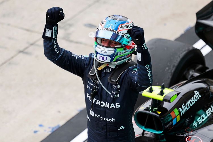 Ein Rennfahrer in vollständiger Rennmontur und Helm jubelt mit erhobenen Fäusten neben einem schwarzen Formel-1-Auto mit Mercedes-Branding. Der Moment findet auf der Boxengasse während des Großen Preises der USA 2026 in Austin statt.