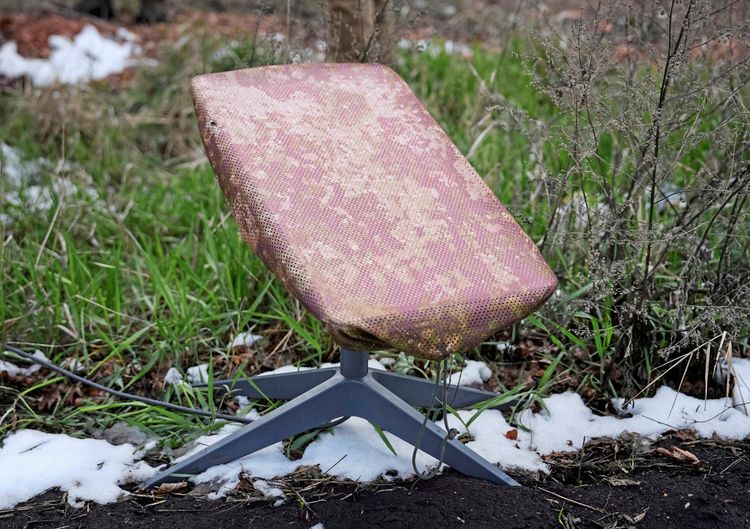 Ein Starlink-Satelliteninternet-System mit einem leicht beschädigten, fleckigen Gehäuse ist auf einer verschneiten und grasbewachsenen Fläche in der Nähe der Frontstadt Pokrowsk in der Region Donezk, Ukraine, aufgestellt.