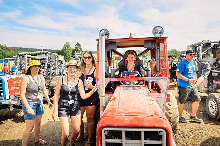 Eine Frau sitzt in einem roten Traktor, links daneben stehen drei weitere Frauen