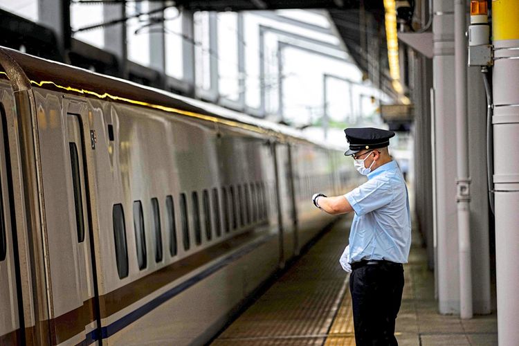 Ein Angestellter von Japan Railways schaut auf seine Uhr, während er neben einem Shinkansen-Hochgeschwindigkeitszug in einem Bahnhof steht