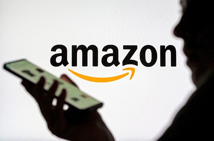 Frau mit Smartphone vor angezeigtem Amazon-Logo zu sehen