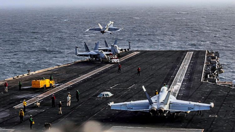 Eine F/A-18E Super Hornet startet von der Flugdeckoberfläche des Flugzeugträgers der Nimitz-Klasse USS Abraham Lincoln. Weitere Flugzeuge und Besatzungsmitglieder sind auf dem Deck zu sehen. Im Hintergrund das offene Meer.