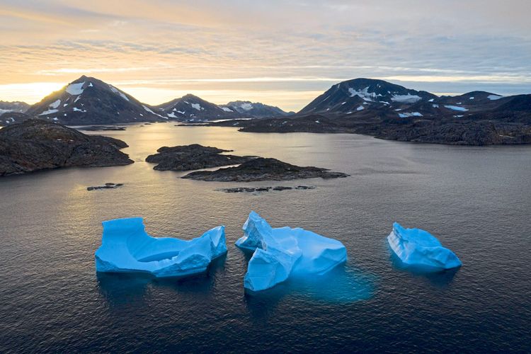 Drei einzelne Eisberge zwischen Schäreninseln, im Hintergrund leicht schneebedeckte Berge