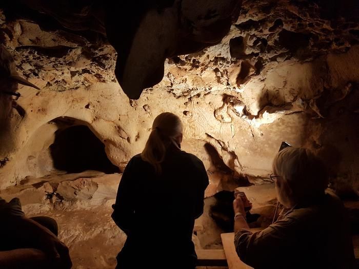 Zwei Fachleute von hinten vor der Höhlenwand, angeleuchtet sind im Hintergrund Linien zu erkennen, die Neandertaler in die Wand graviert haben.