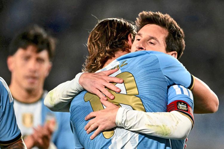 Zwei argentinische Fußballspieler umarmen sich während eines Spiels im Mas Monumental-Stadion in Buenos Aires. Einer trägt die Nummer 18, der andere die Nummer 10 und eine Kapitänsbinde. Im Hintergrund ist ein weiterer Spieler zu sehen.