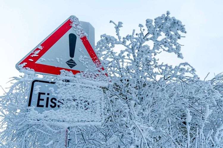 Schneebedecktes Warnschild auf Straße, vom Schriftzug ist nur 