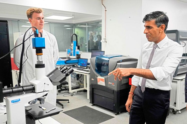 Der britische Premierminister Rishi Sunak steht neben einem Wissenschafter in einem Labor und deutet auf ein Mikroskop
