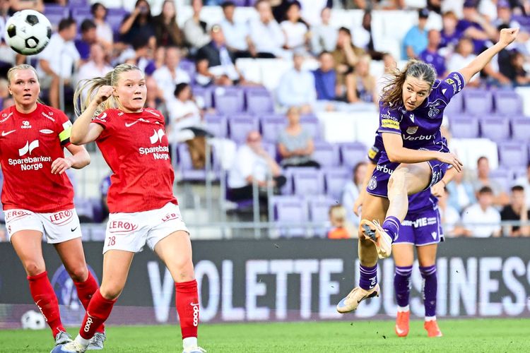 Eine Szene aus einem Frauenfußball-Spiel: Eine Spielerin des FK Austria Wien in lila Trikot schießt den Ball, während zwei Spielerinnen von Brann Bergen in roten Trikots versuchen zu blocken. Im Hintergrund sind Zuschauer auf den Rängen der Generali-Arena in Wien zu sehen.