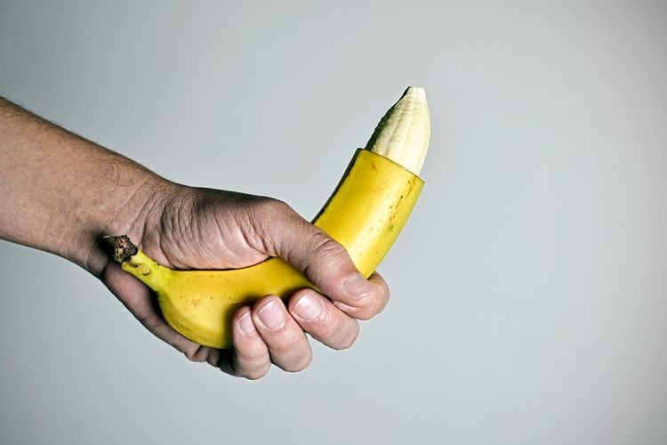 Mann hält eine Banane in der Hand, an deren Spitze die Schale fehlt