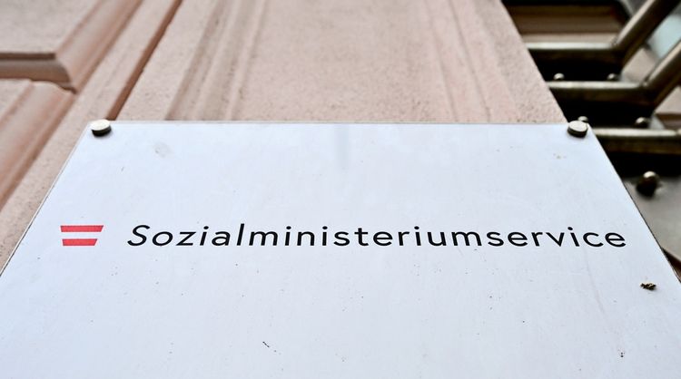 Eine Beschilderung mit der Aufschrift „Sozialministeriumservice“ und einem rot-weiß-roten Symbol, montiert an einer hellen Wand.