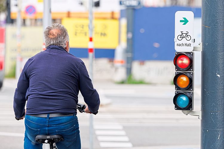 Eine Person auf einem Fahrrad wartet bei einer Ampel, die mit einem Zusatzschild ausgestattet ist die das Abbiegen bei Rot erlaubt