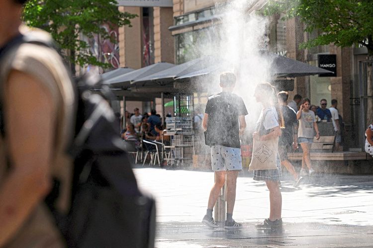 Zwei Menschen suchen Abkühlung unter einer Nebendusche während einer Hitzewelle in der Wiener Innenstadt am 21. August 2023