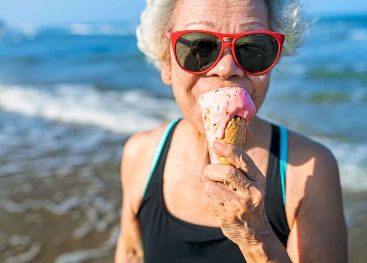Alte Frau mit roter Sonnenbrille isst Eis am Meer