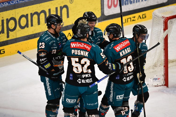 Eishockeyspieler eines Teams in türkisfarbenen Trikots feiern ein Tor auf dem Eis. Im Hintergrund ist ein Tor und Werbebanden zu sehen.