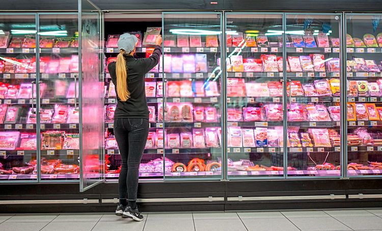 Mitarbeiterin in einem Supermarkt vor einem Kühlregal stehend, Produkte schlichtend