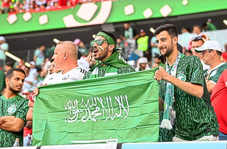 Saudische Fußballfans jubeln mit Flagge.