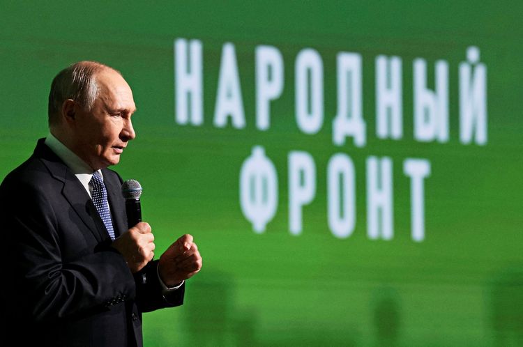 Wladimir Putin vor einem grünen Plakat, auf dem 