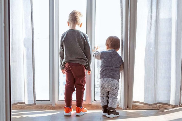 Zwei Kinder sind von hinten zu sehen und schauen durch ein Fenster hinunter auf die Straße