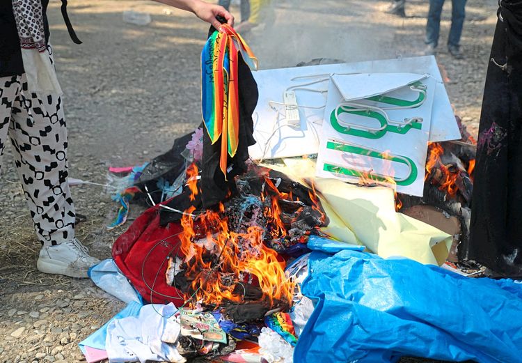 Eine Frau wirft eine Regenbogenfahne in ein Feuer