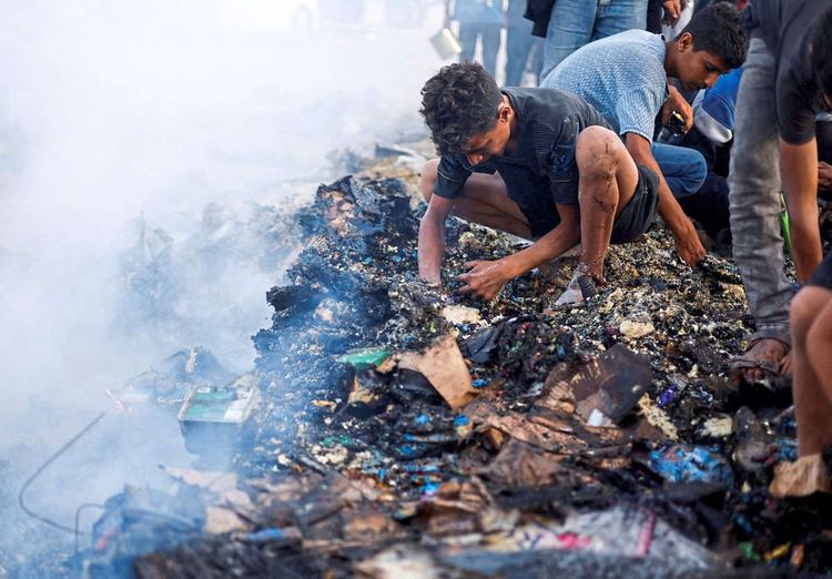 Ein Mann kniet über einem Haufen verbrannter Gegenstände.